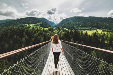 Ormanlara giden bir uçurumun üzerinde tahta bir köprüde yürüyen bir kadın. İsviçre