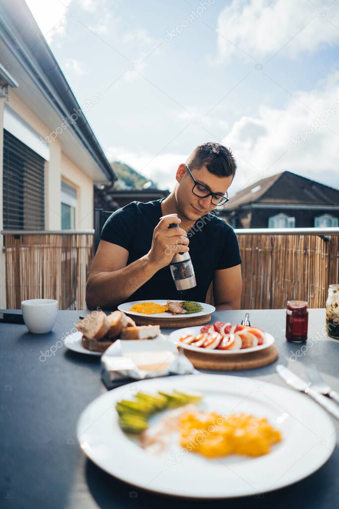 Man having breakfast on the balcony in the fresh air. Scrambled eggs, mozzarella, tomatoes, avocado and lettuce.