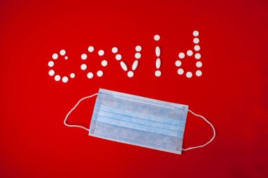 Kırmızı arka planda kapak hapları ve tıbbi maske.