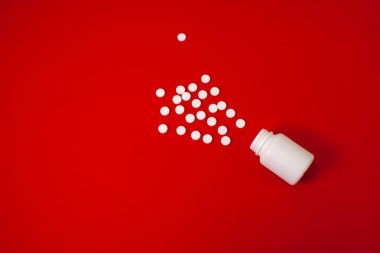 Kırmızı arka planda beyaz haplar ve bir kavanoz haplar.