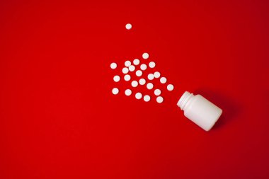 Kırmızı arka planda beyaz haplar ve bir kavanoz haplar.