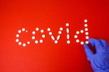 Kırmızı arka planda mavi eldivenli kapalı haplar.