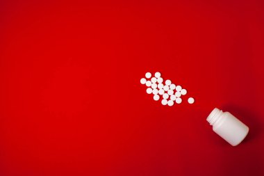 Kırmızı arka planda beyaz haplar ve bir kavanoz haplar.