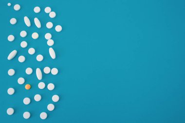 mavi-yeşil zemin üzerinde bir turuncu tablet içeren yuvarlak beyaz tabletler ve kapsüller, tabletler görüntünün sol tarafında yer almaktadır, metin için boş bir alan