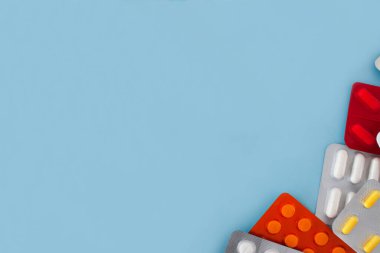 Renkli tabletler ve kapsüller, paketin içindeki tabletler, mavi arkaplan üzerinde eşit olarak dağıtılır, solda ve merkezde metin için boş alan bulunur.