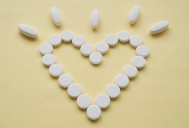 İçi boş kalp şeklinde yuvarlak beyaz haplar. Pembe arka planda bir uyarı var. Haplar kavramsal bir görüntünün merkezinde izole edilmiş.