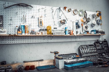 El aletleriyle Moto atölyesi. Anahtarlı tezgah, tornavida, ploskop, elektrik bandı, duvarda koli bandı. Motosiklet parçaları olan masa, mengene. Katılımcı ve otomobil tamircisi için çalışma alanı
