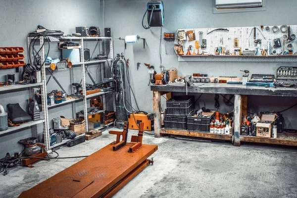 Garage, service area for disassembling, repairing motorcycles, car service station. Inside the workshop with a large workbench and shelving, a huge number of tools for processing wrenches on the wall