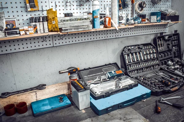 Dentro del taller. Banco de trabajo grande y herramientas para trabajar en el primer plano de la mesa. Espacio de trabajo para mecánico con llaves, alicates en una pared metálica. Garaje para reparación de motocicletas, estación de servicio de automóviles . — Foto de Stock