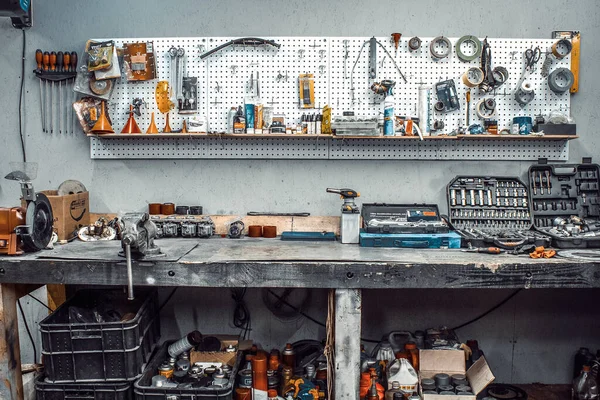 Moto workshop with hand tools. Workbench with sets of keys, screwdrivers, ploskobets, electrical tape, duct tape on the wall. Table with motorcycle parts, vise. Workspace for a joiner, auto mechanic — Stock Photo, Image