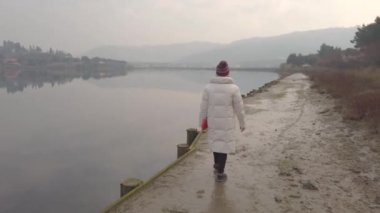Gölün kıyısında gezinen bir kız. Rıhtımda yürürken su gökyüzünü yansıtır..