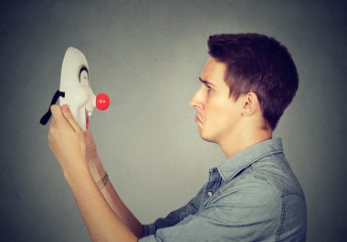 mutlu palyaço maskesi bakarak tutan üzgün adam  