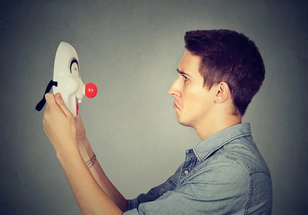 Uomo triste tenendo guardando maschera clown felice — Foto Stock