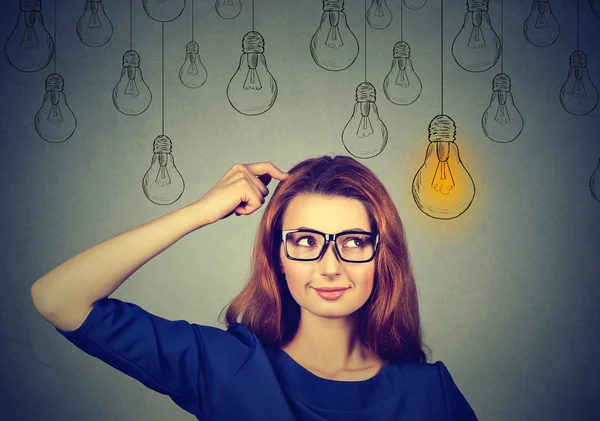 Woman in glasses looking up light idea bulb above head — 스톡 사진