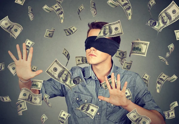 Blindfolded man trying to catch dollar bills banknotes flying in air — Stock Photo, Image
