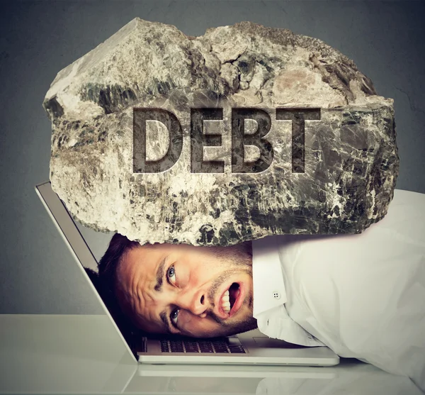 Man squeezed between laptop and rock. Student loan debt concept — Stock Photo, Image