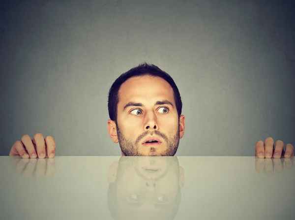 Worried man looks at something peeking from under the table — Stock Photo, Image