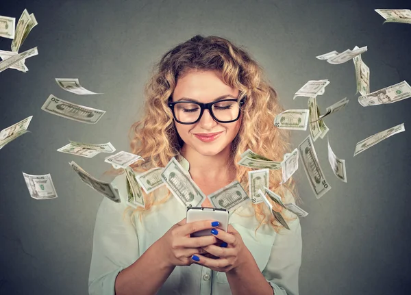 Mujer usando teléfono inteligente con billetes de dólar que vuelan lejos de la pantalla — Foto de Stock