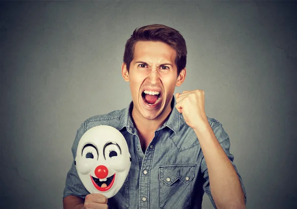 Angry screaming man holding clown mask expressing cheerfulness — ストック写真