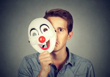 Young sad man hiding behind happy clown mask  clipart