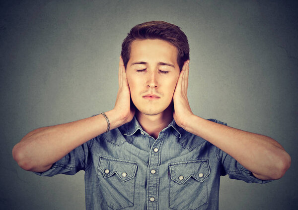 спокойный, расслабленный молодой человек закрывает уши, глаза закрыты
