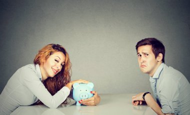 Happy wife with piggy bank sitting across the table from sad husband clipart