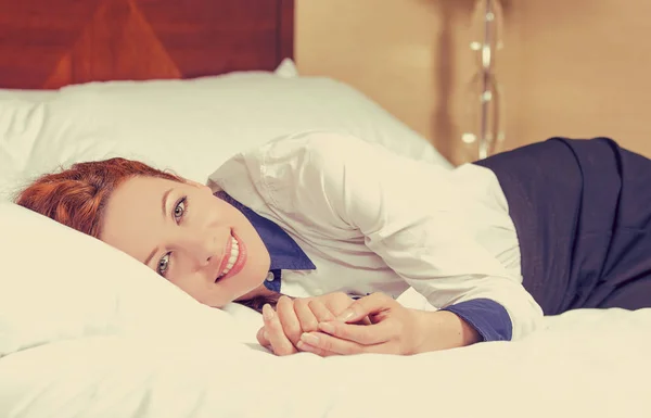 Atrakcyjna młoda kobieta uśmiechający się leżąc w łóżku i patrząc na kamery — Zdjęcie stockowe