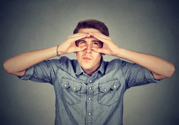 Unzufriedener junger Mann blickt durch Finger wie Ferngläser — Stockfoto