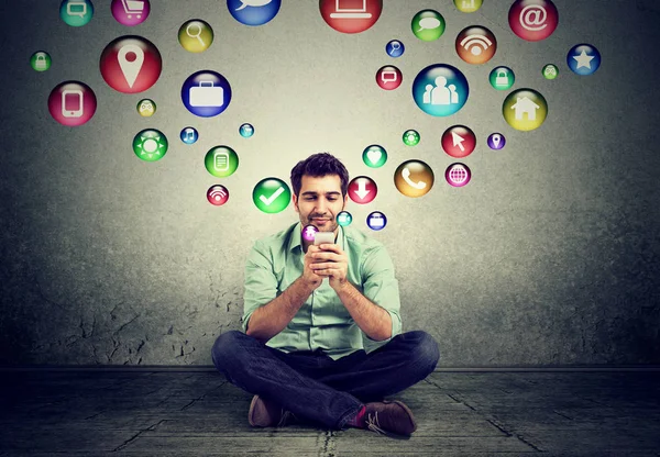 Man sitting on floor using smartphone application icons flying up — Stock Photo, Image