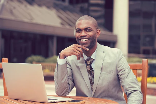 Cheerful business man sitting at table with laptop outside corporate office