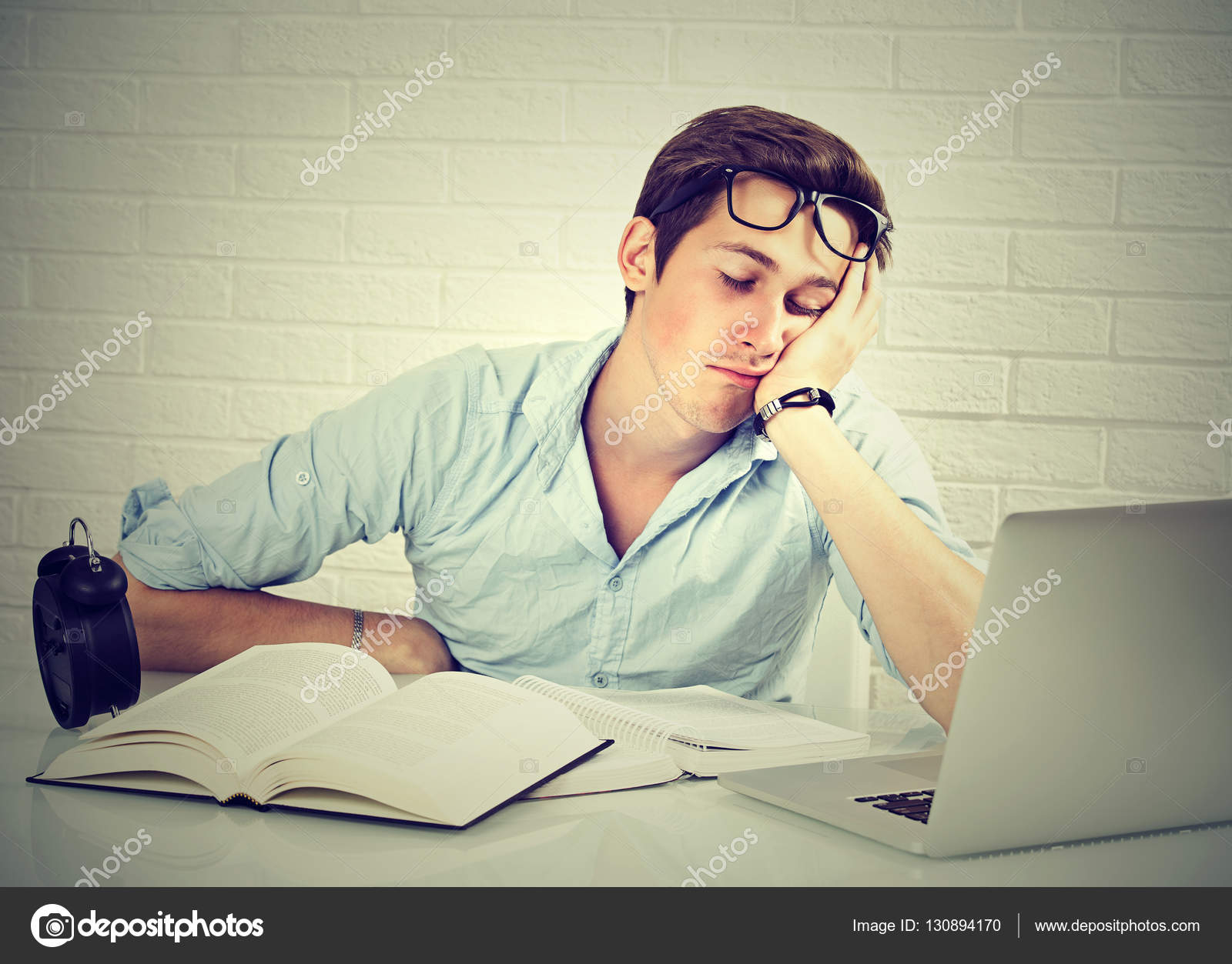 Tired Sleepy Man Sitting At Desk With Books In Front Of Laptop