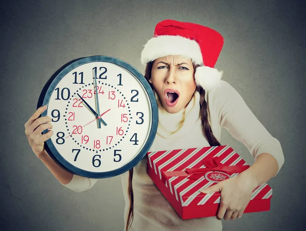 Stressed in a hurry woman wearing santa claus hat holding clock gift box — Stock Photo, Image