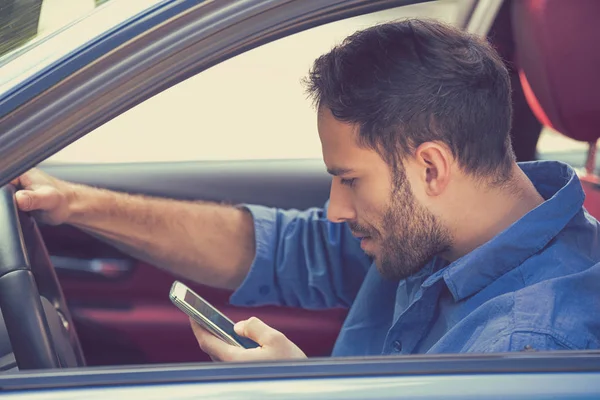 Молодой бизнесмен, использующий СМС на мобильном телефоне во время вождения автомобиля — стоковое фото