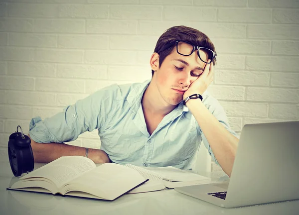 Уставший сонный мужчина сидит за столом с книгами перед ноутбуком — стоковое фото