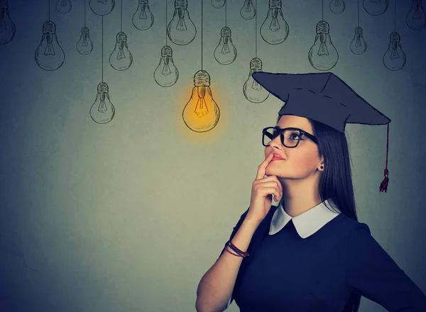 Nachdenkliche Studentin im Mützenmantel, die zum Glühbirnendenken aufschaut — Stockfoto