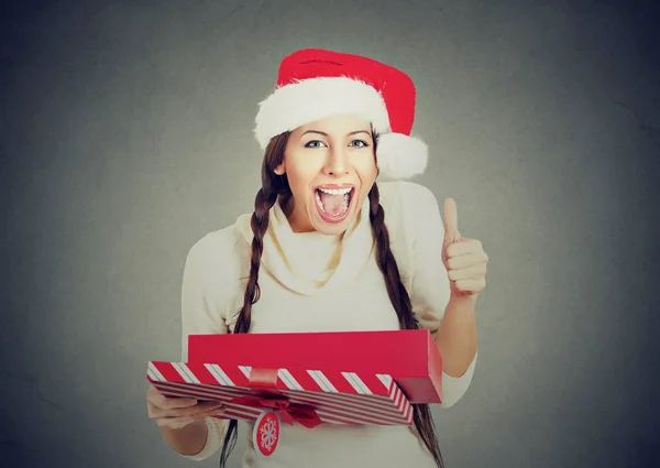 Woman wearing santa claus hat opening gift box showing thumbs up — Stock Photo, Image