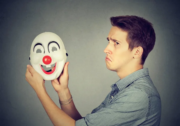 Jeune homme triste avec un masque de clown heureux. Les émotions humaines — Photo