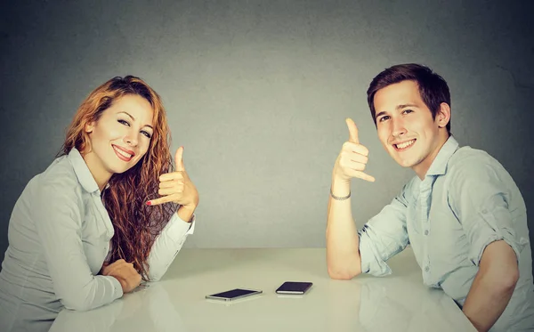 Man and woman with call me hand gesture sitting at table — Stock Photo, Image