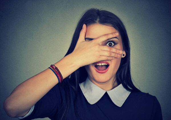 Удивлённая женщина смотрит между пальцами
