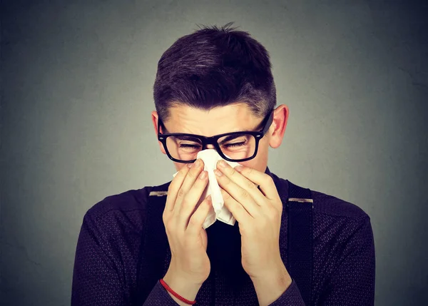 Man in glasses sneezing in a tissue blowing runny nose — Stock Photo, Image