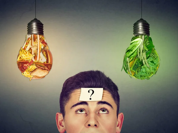 Людина з питанням дивиться на нездорову їжу овочі лампочки — стокове фото