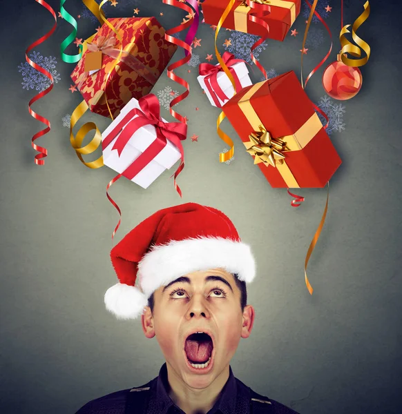 Surprised man in santa claus hat looking up at multiple christmas gifts — Stock Photo, Image