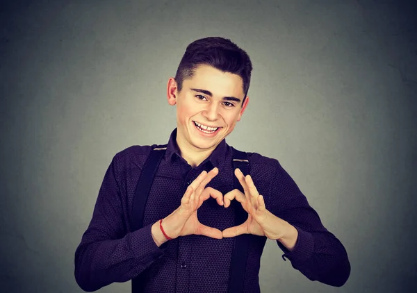 Knappe lachende jongeman maakt hart vorm met vingers handen — Stockfoto