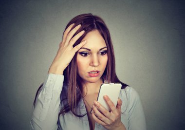 Upset woman looking at cellphone worried with message she received clipart