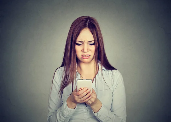 Расстроенная женщина, глядя на сотовый телефон, недовольна сообщением, которое получила — стоковое фото