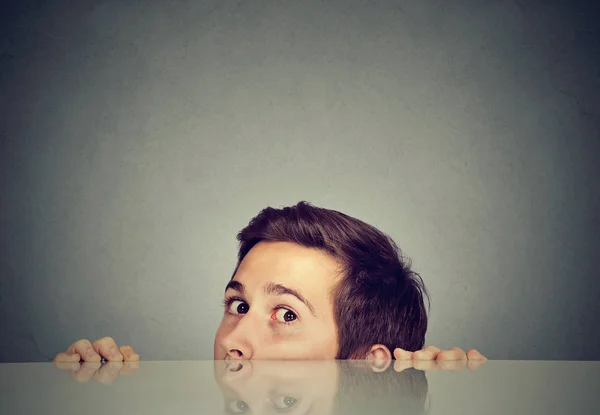Suspicious scared man peeking from under the table hiding — Stock Photo, Image