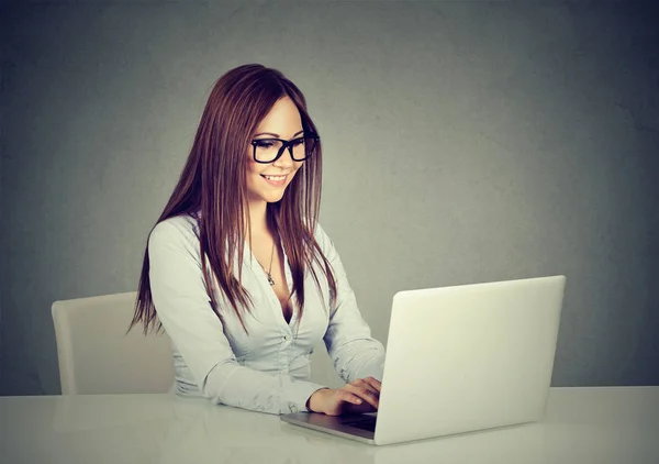 Женщина, сидящая за столом и работающая на ноутбуке, улыбается — стоковое фото