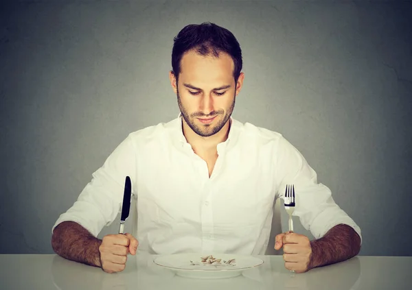 Человек с вилкой и ножом сидит за столом и смотрит на пустую тарелку — стоковое фото