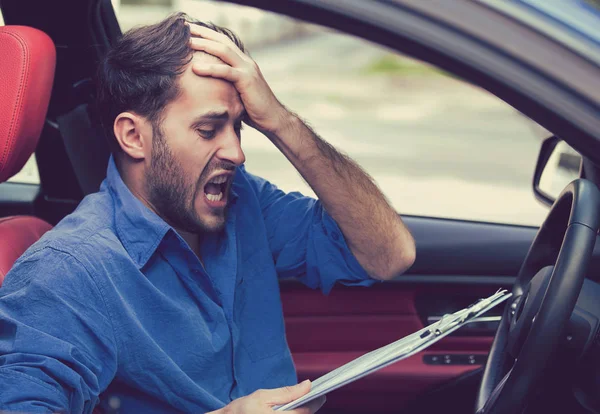 Zoufalý mladík řidič zatížené papíry sedí uvnitř jeho auto - Stock obrázek