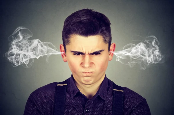 Сердитый молодой человек, выдувающий пар из ушей — стоковое фото